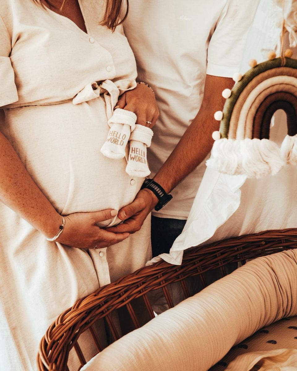 Babybauch mit Babysocken neben einem Korbbettchen
