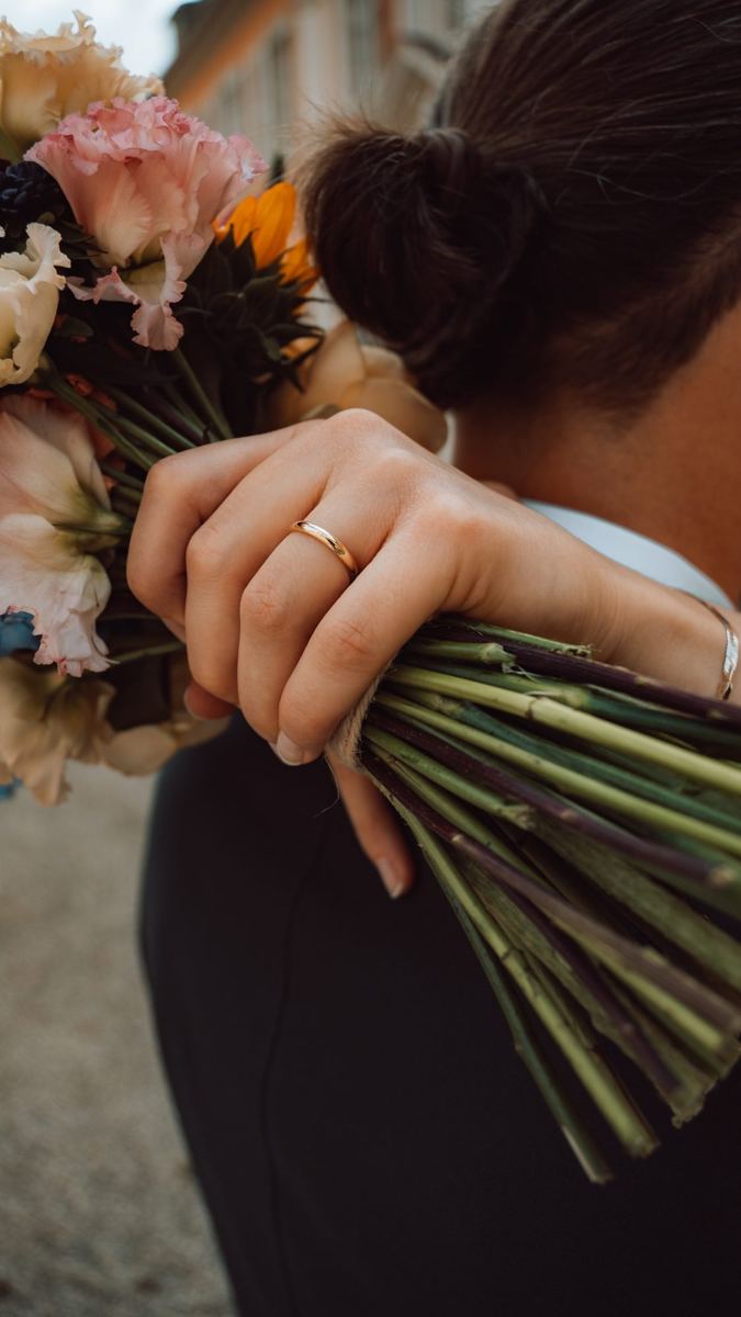Braut hält ihren Blumenstrauß über der Schulter, der Ehering im Fokus